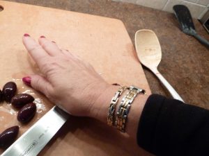 Pressing down on the flat of a knife blade to split an olive to remove its seed