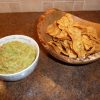 Bowl of guacamole next to a serving dish of tortilla chips
