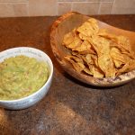 Bowl of guacamole next to a serving dish of tortilla chips