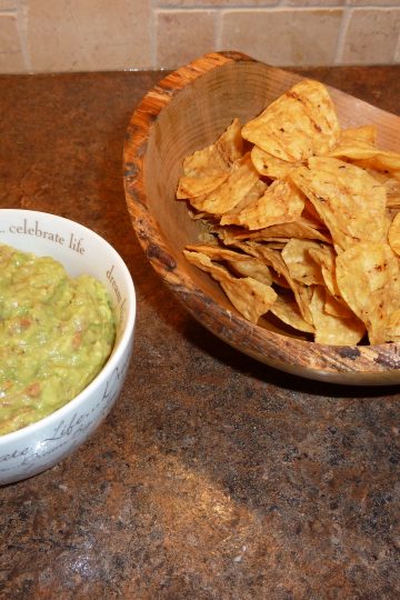 Bowl of guacamole next to a serving dish of tortilla chips