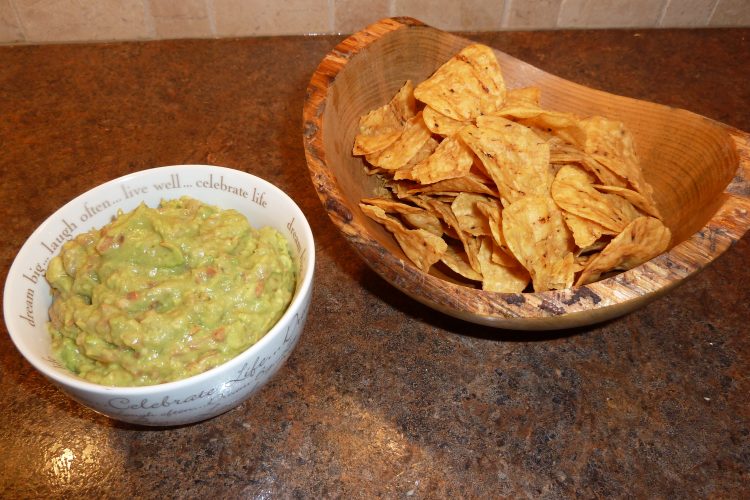 Bowl of guacamole next to a serving dish of tortilla chips