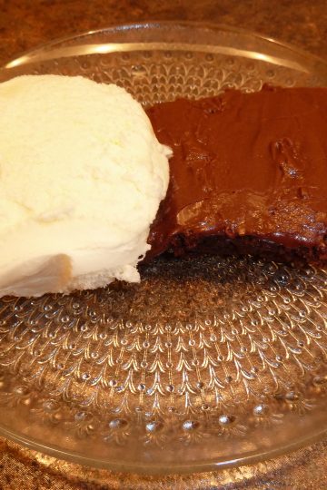 shows a chocolate brownie on a plate with a side serving of ice cream