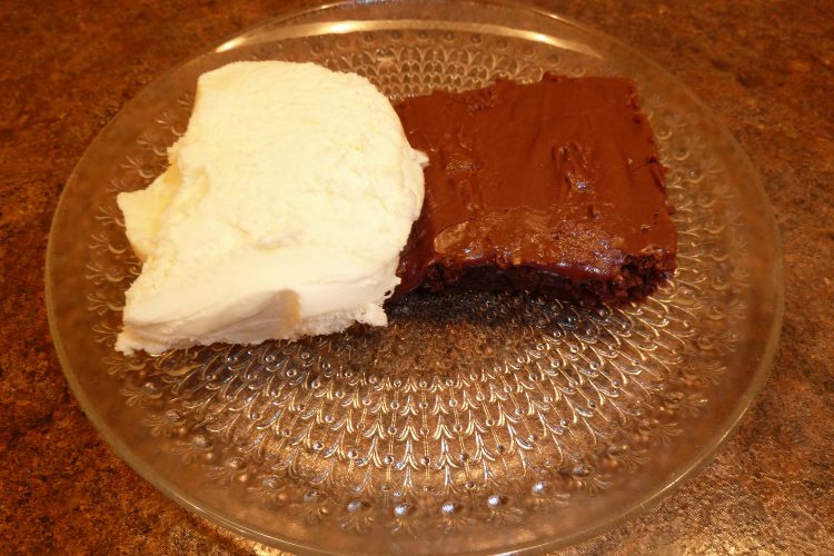 shows a chocolate brownie on a plate with a side serving of ice cream