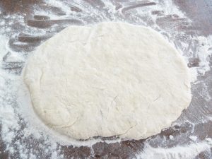 Biscuit dough flattened on a floured countertop